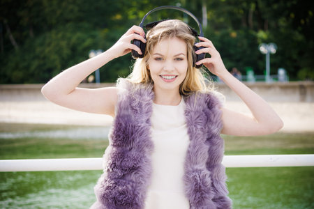 Happy joyful woman listening to music while being outdoor. Teenage female wearing headphones having...