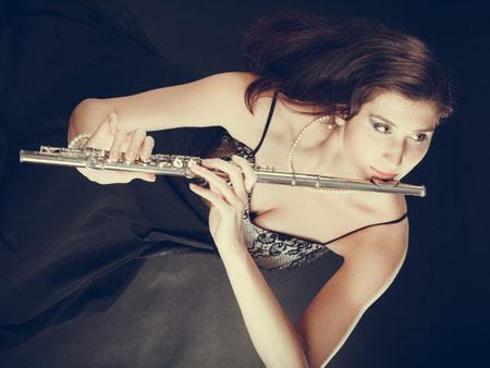 Music and elegance. Alluring elegant woman playing on transverse flute. Female musician with her...