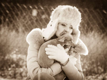 Young woman having fun during winter. Female playing with her small purebreed dog puppy while snow is snowingの写真素材