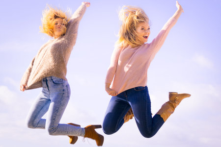 Two women full of joy jumping around with sky in background. Female friends having fun outdoor.