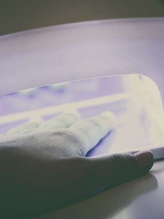 Woman hand in uv led lamp drying gel hybrid manicure on nails. Beauty wellness spa treatment concept.の写真素材