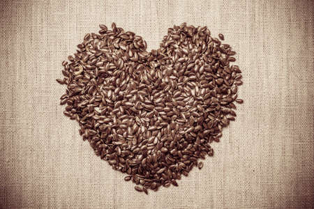 Diet healthcare healthy food. Raw flax seeds linseed heart shaped on sack burlap background.の写真素材