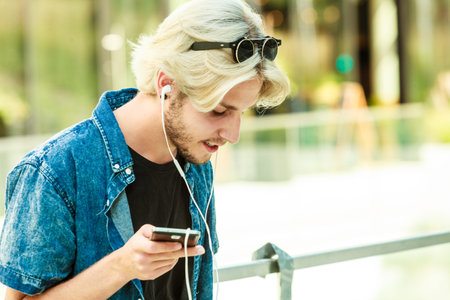 Men fashion, technology, urban style clothing concept. Hipster guy standing on city street wearing...