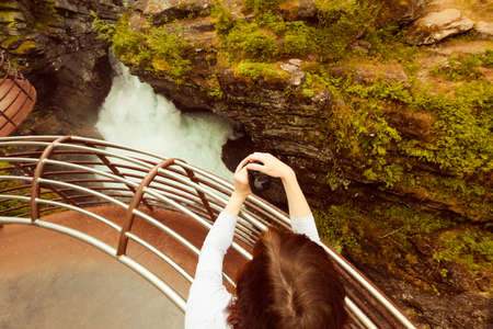 Tourist attraction in Norway, Europe. Woman photographer taking photo with camera on Gudbrandsjuvet viewpoint, Valldalen valley, between Valldal and Trollstigen.の写真素材