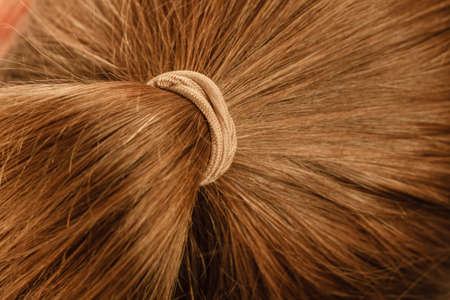 Detailed close up of brown, dark blonde hair in ponytail with band. Hairdo surface.の写真素材