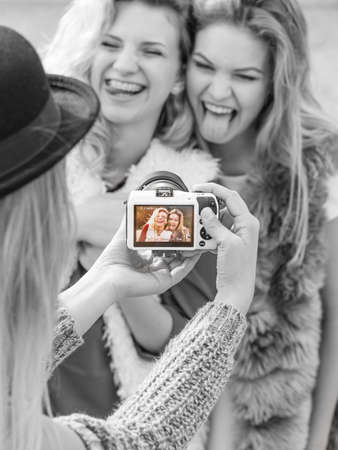 Three females friends having fun during outdoor photo session. Woman taking pictures of two during warm autumn weather.の写真素材