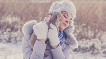 Young woman having fun during winter. Female playing with her small purebreed dog puppy while snow is snowingの写真素材