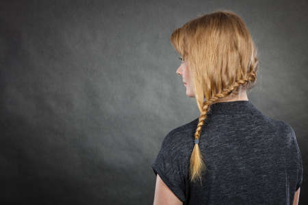 Hairstyles and hairstyiling concept. Woman with dark blonde hair and braid hairdo, back view. Studio shot on dark backgroundの写真素材