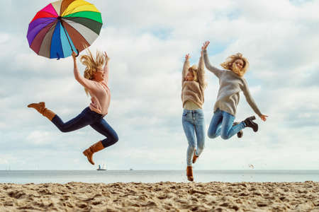 Three women full of joy jumping around with colorful umbrella. Female friends having fun outdoor.の写真素材