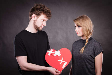 Broken heart difficult love concept. Sad unhappy couple woman and man holding paper red heart fixed with plaster bandage. Rift in relations.の写真素材