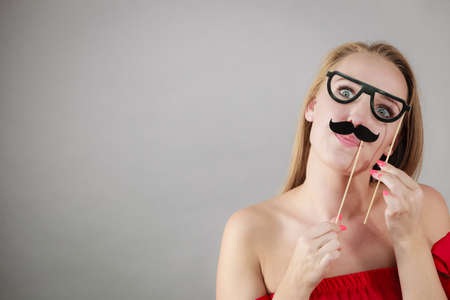 Happy woman holding fake moustache on stick having fun. Photo and carnival funny accessories concept.の写真素材