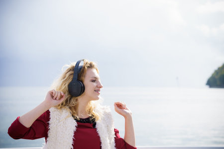 Happy joyful woman listening to music while being outdoor. Teenage female wearing headphones having fun on a walk.の写真素材