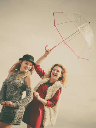Two fashionable women wearing stylish outfits holding transparent umbrella spending their free time outdoorの写真素材