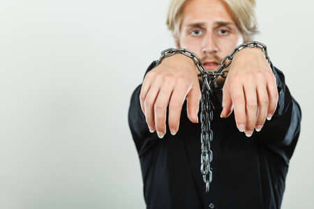 No freedom, social problems concept. Sad man with chained hands, studio shot on light grey backgroundの写真素材