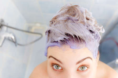 Woman applying coloring shampoo on her hair. Female having purple washing product. Toning blonde color at home.の写真素材