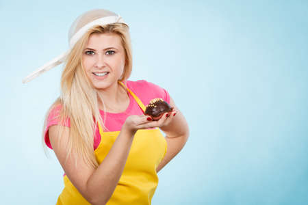 Baking tasty desserts sweets at home concept. Woman holding delicious sweet chocolate cupcake wearing apron and colander on head as hat.の写真素材