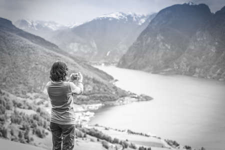 Tourism and travel. Woman tourist taking photo with camera, enjoying mountains fjords view in Sogn og Fjordane county. Norway Scandinavia, black and white photoの写真素材