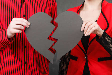 Bad relationship, breaking up, divorce concept. Man and woman holding broken heart made of black paper.の写真素材