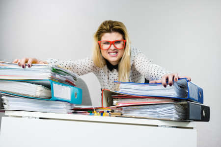 Focused business woman feeling energetic sitting working at desk full off documents in binders.の写真素材