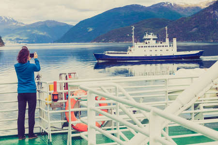 Tourism vacation and travel. Tourist woman on cruise ship enjoying fjord view, taking photo with camera. Norway Scandinavia Europe. Norddalsfjorden as seen from ferry.の写真素材
