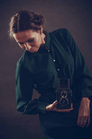 Woman retro style long dark gown taking picture with old camera, vintage photo