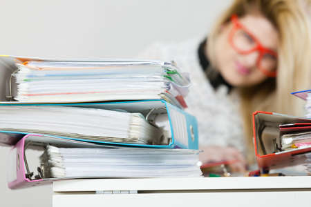 Business woman doing her work sitting working at desk full off documents in binders.の写真素材