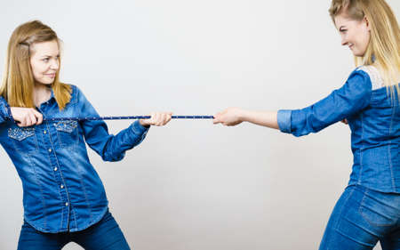 Two women wearing jeans outfit having fun pulling rope, good rivalry concept. Sporty competition.の写真素材