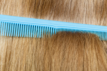 Combing and brushing concept. Routine everyday hygiene. Close up of detail blue comb in blonde smoothy healthy female hair. の写真素材