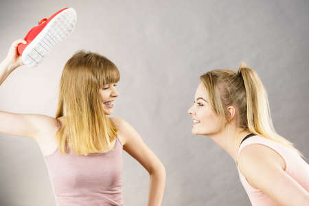 Agressive women having argue fight using shoes, female friend being scared. Violance concept.の写真素材