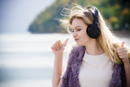 Happy joyful woman listening to music while being outdoor. Teenage female wearing headphones having...