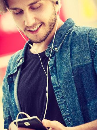 Men fashion, technology, urban style clothing concept. Hipster smiling guy standing on city street...