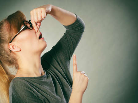 Filth hygiene dirt trash garbage concept. Nerdy girl holding nose. Young blonde in glasses pinching to stop odor. Bad disgusting smell.の写真素材