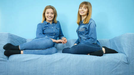 Friendship, human relations concept. Two happy women friends or sisters wearing jeans shirts sitting on sofa having fun.の写真素材