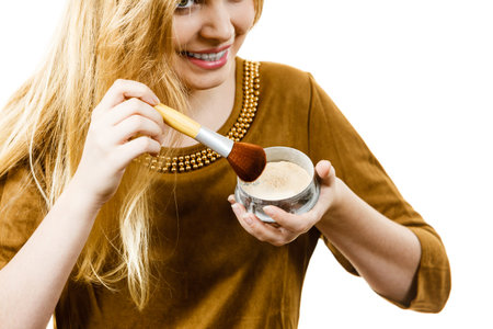 Fashionable cheerful young female holding professional powder brush, adding last touch to her make...