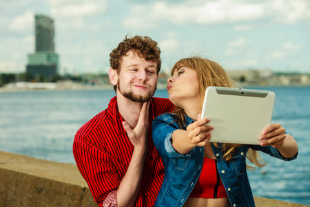 Technology holidays and happiness concept. Young couple taking self picture selfie with tablet...