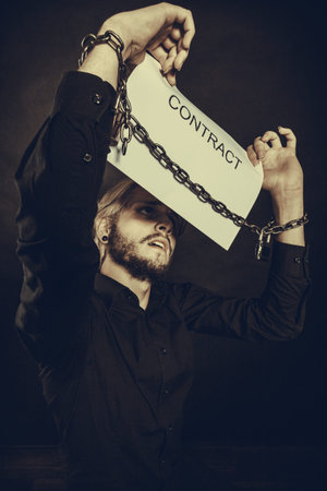 Stress at work, no freedom, pursuit of money concept. Scared man with chained hands holding...