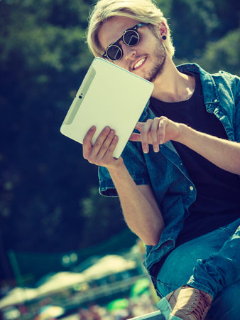 Contacts, technology concept. Hipster young blonde man on vacations holding his tablet checking...