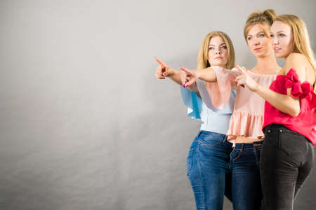 Fashionable adult female friends models pointing at grey copy space. Studio shotの写真素材