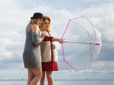 Two fashionable women wearing stylish outfits holding transparent umbrella spending their free time outdoorの写真素材