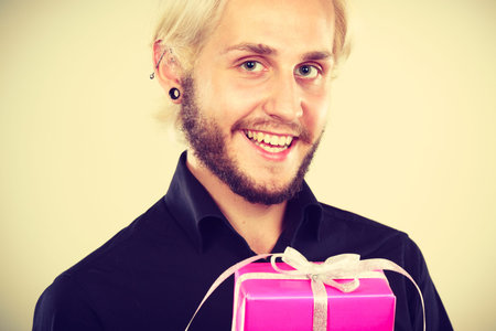 People celebrating xmas, love and happiness concept - cool young man holding present pink gift box in handの写真素材