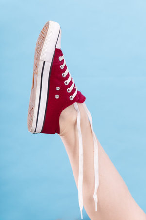 Footwear, fashion, shoes concept. Person tying laces in red sneaker with foot up, studio shot on...