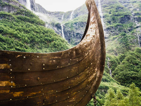 Part of old wooden viking boat in norwegian nature, mountains with waterfalls in the background. Tourism and traveling conceptの写真素材