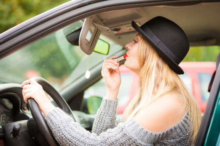 Young attractive woman looking in rear view mirror painting her lips doing applying make up while driving the car.の写真素材
