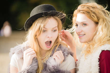 Two fashionable women wearing stylish outfits during warm autumnal weather gossiping together.の写真素材