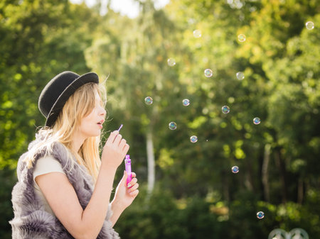 Funny young fashionable hipster teenage woman blowing soap bubbles outdoor having fun.