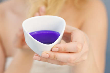 Woman pouring purple hair dye or shampoo toner into white bowl. Hygiene object concept.の写真素材