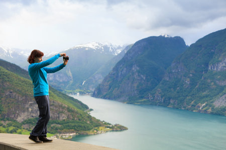 Tourism and travel. Woman tourist taking photo with camera, enjoying mountains fjords view in Sogn...