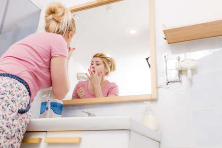 Woman looking at her reflection in mirror thinking about her complexes having serious face expression, analyzing face skin complexion.の写真素材