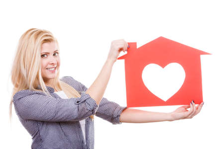 Ownership and property concept. Happy woman holding red paper house with hole in heart shape, loving new home.の写真素材