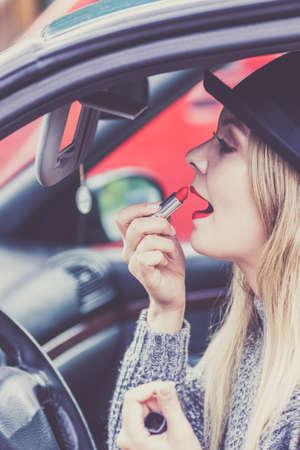 Young attractive woman looking in rear view mirror painting her lips doing applying make up while driving the car.の写真素材